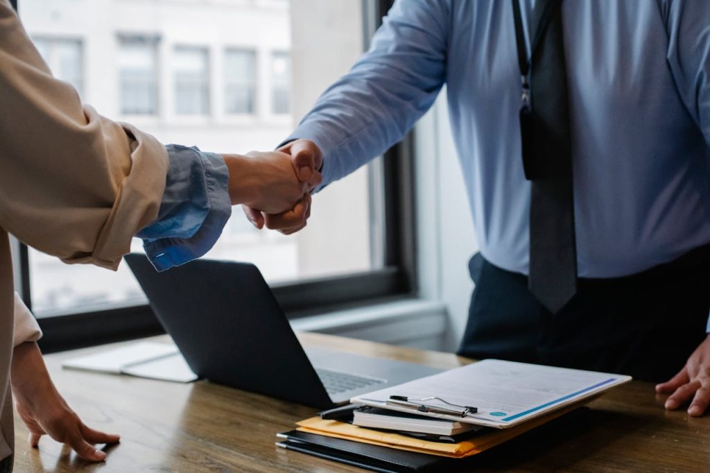 crop-colleagues-shaking-hands-in-office-5673488 Crop unrecognizable coworkers in formal wear standing at table with laptop and documents while greeting each other before meeting